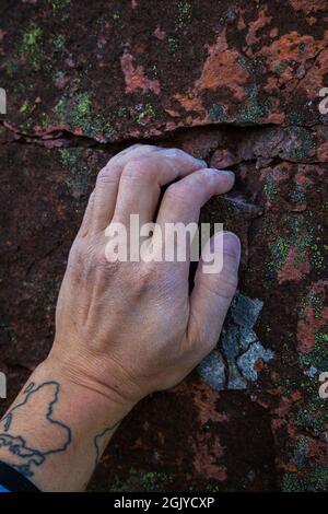 Primo piano di una mano calciosa di un arrampicatore che afferra una piccola presa su una roccia. Foto Stock