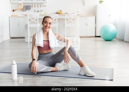 Soddisfatto europeo grazioso giovane blonde fitness blogger riposo dopo l'allenamento a casa con l'acqua Foto Stock