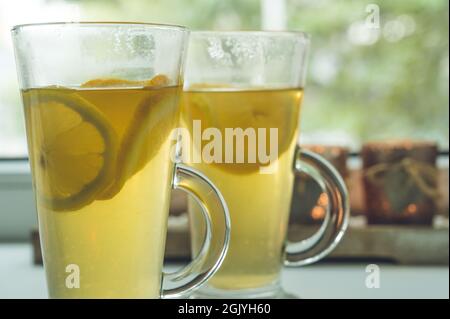 Primo piano di un paio di bicchieri con tè verde vitaminico con limone e arancia. Candele sullo sfondo. Bevanda calda sana. Foto Stock