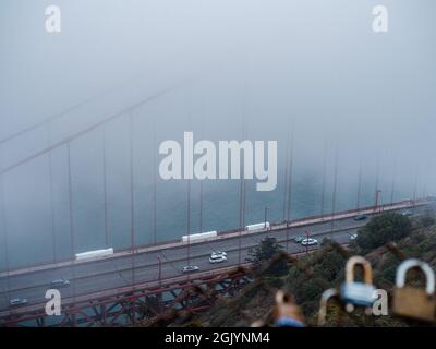 Golden Gate Bridge in estate tipica nebbia con auto che attraversano sotto visto dietro una recinzione di lucchetti d'amore Foto Stock