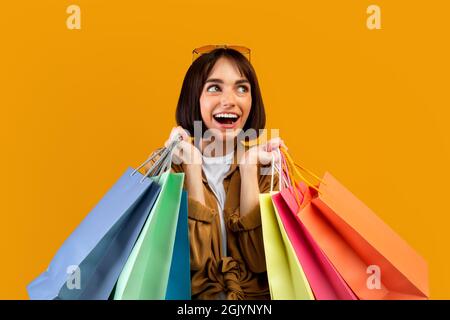 Concetto di vendita stagionale e shopaholic. Donna eccitata che tiene lotto dei sacchetti luminosi di shopping e guardando da parte Foto Stock