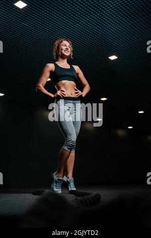Felice atleta femminile si leva sullo sfondo di una sala nera. Foto Stock