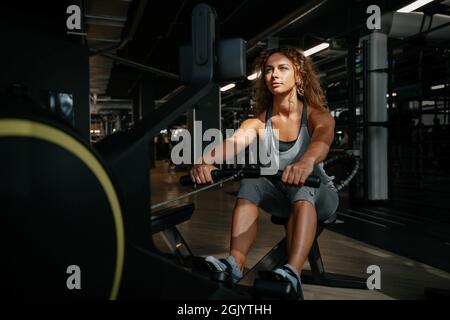 La donna atletica è impegnata in forma fisica su una macchina per il remi in palestra. Foto Stock