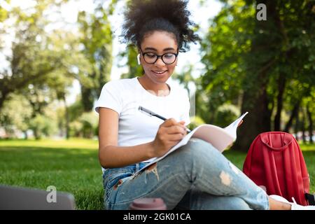 Studentessa africana imparare usando il laptop e prendere appunti all'aperto Foto Stock