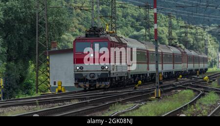 Treno passeggeri con locomotiva elettrica rossa e pullman passeggeri rossi in serata estiva Foto Stock