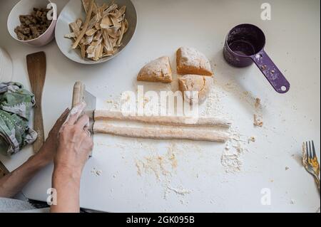 Vista dall'alto di una donna che fa deliziosi gnocchi italiani freschi su un banco da cucina con farina polverata. Foto Stock