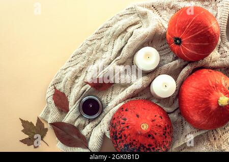 Autunno piatto posato con zucche, foglie, candele su un maglione a maglia. Sfondo beige, vista dall'alto. Foto Stock