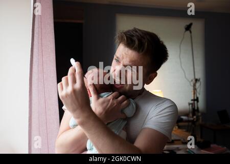 Preoccupato il padre di un'unga che guarda il termometro che tiene il suo neonato nelle mani. Foto Stock