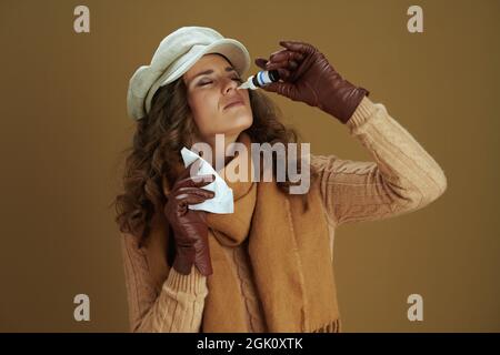 Ciao settembre. Donna moderna di 40 anni in sciarpa con fazzoletti di carta, sparatutto nasale e guanti di pelle isolati sul beige. Foto Stock