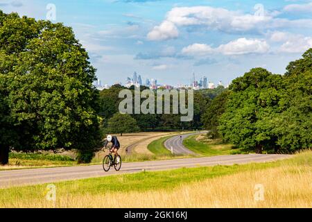Un ciclista solitario fa ciclare una ripida collina a Richmond Park nel sole estivo con uno sfondo della City of London Foto Stock