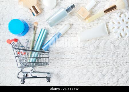 piatto invernale con cosmetici, fiocco di neve e carrello su sfondo bianco lavorato a maglia. Foto Stock