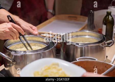 Lo chef prepara la pasta in grandi padelle metalliche. Le mani maschili spalmano la pasta su un piatto. Primo piano. Foto Stock