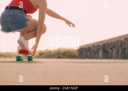 Primo piano di una giovane donna in skateboard nel parco skate. Concetto di sport e lifestyle. Focus su piede e longboard rosso. Foto Stock