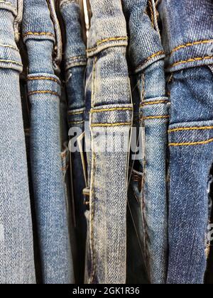 Fila di nuovi jeans blu appesi sul portabiti del negozio Foto Stock