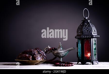 Concetto di cibo e bevande Ramadan. Frutta dadari, lanterna ramadan con lampada araba e rosario in legno su un tavolo di legno su sfondo scuro. Foto Stock