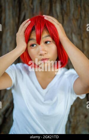 Red Blood Cell Cosplay attrice in piedi con Redwood Tree | ragazza asiatica teen con Red Wig Foto Stock