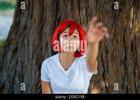 Red Blood Cell Cosplay attrice in piedi con Redwood Tree | ragazza asiatica teen con Red Wig Foto Stock