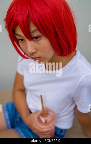 Red Blood Cell Cosplay attrice seduto bere uno Smoothie | Asian Teenage Girl in Red Wig Foto Stock