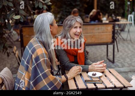 La signora anziana ride passando il tempo con l'amico a tavola con caramelle in Street cafe Foto Stock