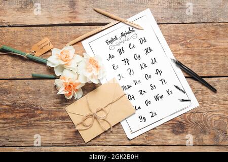 Carta con alfabeto, penne, buste e fiori su sfondo di legno Foto Stock