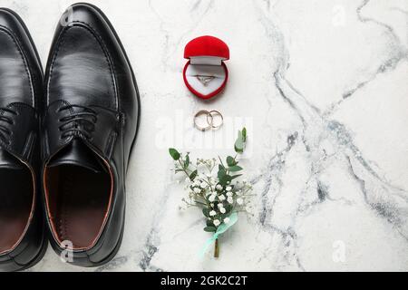 Scarpe maschili, bellissimi fiori, anelli per matrimoni e fidanzamento su sfondo di marmo chiaro Foto Stock