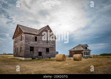 Due case abbandonate, balle di fieno e un'auto classica nella città fantasma di Robsart, Saskatchewan Foto Stock