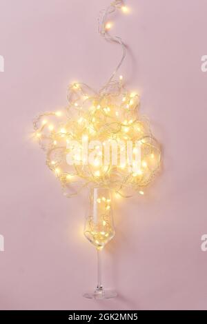 Bicchiere di vino e ghirlanda con lampadine su sfondo rosa minimo concetto creativo festa. Foto Stock