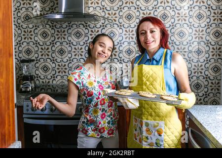 Madre latina e sua figlia adolescente con paralisi cerebrale in cucina cottura biscotti in America Latina disabilità concetto Foto Stock