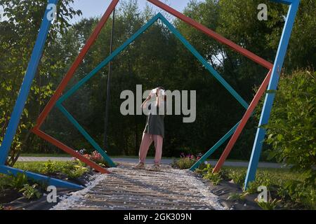 La ragazza tiene gli occhiali di realtà virtuale sulla sua testa con le mani, si leva sullo sfondo di tubi di ferro ad arco. Il concetto del futuro. Foto di alta qualità Foto Stock