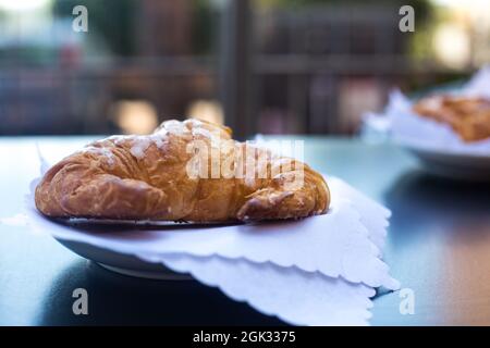 Colazione italiana. Cornetto o cornetto fresco croccante servito in terrazza all'aperto su tovaglioli bianchi con vista sulla casa vicina in background. Estate Foto Stock