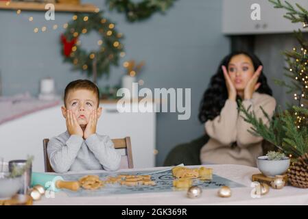 Mamma e figlio fanno i volti e si divertono a preparare i biscotti di Natale in cucina Foto Stock