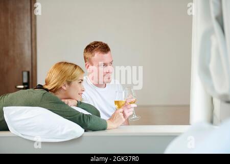 Sorridente giovane coppia che beve champagne e guarda film o programmi tv Foto Stock