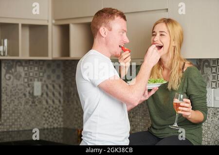 Gioiosa coppia giovane in amore che si nutrono quando si ha una cena romatica a casa Foto Stock