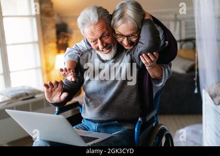Felice coppia anziana che usa il notebook a casa e che si diverte insieme. Concetto di persone tecnologiche Foto Stock