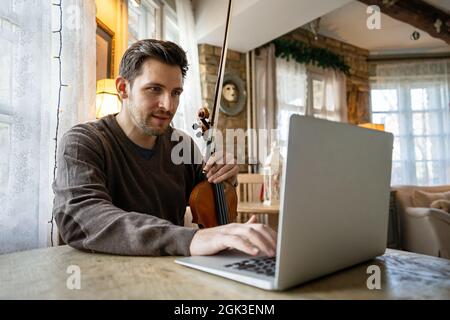 L'uomo studente impara a suonare il violino online utilizzando un computer portatile. Foto Stock