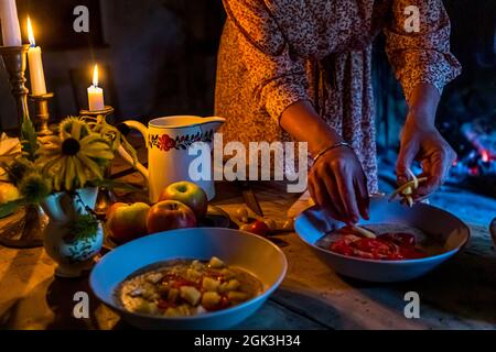 Due ciotole di polenta guarnite con pomodori e formaggio alla luce delle candele sul tavolo a Cà Vegia a Cerentino, mani che aggiungono le ultime strisce. Costruita intorno al 1600, la casa patriziale rinuncia deliberatamente all’elettricità. Circolo della Rovana, Ticino, Svizzera. Foto Stock