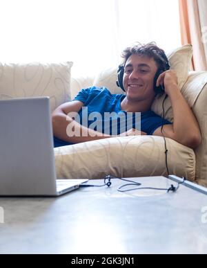 Giovane studente sul divano guardando film con computer portatile - giovani con tecnologia - stile di vita moderno con corsi online e stock pho scuola Foto Stock