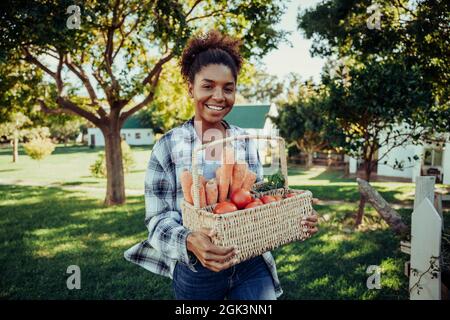 Razza mista femmina a piedi attraverso villaggio fattoria sorridente cercando felice dopo la raccolta di verdure fresche dal giardino Foto Stock