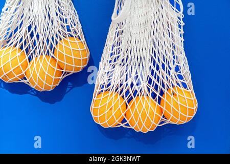 Arance succose in sacchi a rete eco-compatibili su sfondo blu. Foto Stock