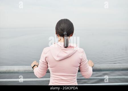 Vista posteriore della giovane donna in piedi sul ponte e guardando la vista del mare bello Foto Stock
