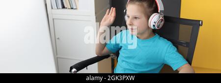 La bambina in cuffia davanti al computer solleva la lezione nel messaggio di saluto Foto Stock