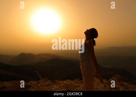 Profilo di una silhouette donna respirando aria fresca in montagna al tramonto Foto Stock