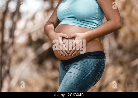 Pancia di una donna incinta. Facendo il cuore forma dalle sue mani su Belly. Parte del corpo. Godere della gravidanza. Giovane Happy Family. Foto Stock