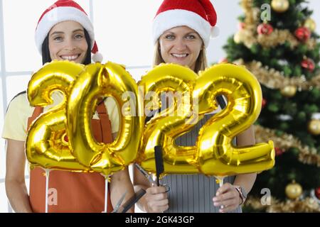 Due donne sorridenti parrucchieri in uniformi tenere numeri 2022 e forbici con pettine Foto Stock