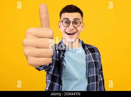 Felice giovane uomo nerd mostrando enorme pollice in su Foto Stock