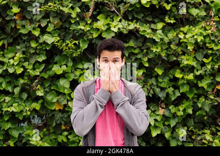 sorpreso adolescente che copre la sua bocca con le mani su uno sfondo verde piante, concetto di espressioni e emozioni umane, copia spazio per il testo Foto Stock