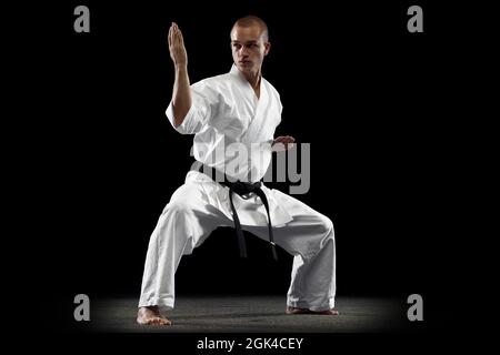 Ritratto a tutta lunghezza del karate giovane allenatore sportivo isolato su sfondo nero. Posa a cavallo Foto Stock