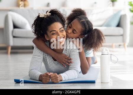 Buona madre nera e figlia coccolarsi mentre praticano lo yoga Foto Stock