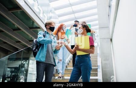 Studenti universitari che camminano lungo le scale e saluto al chiuso, concetto di coronavirus. Foto Stock