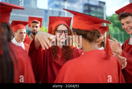 Amici allegri degli studenti universitari che festeggiano e abbracciano all'aperto, concetto di laurea. Foto Stock